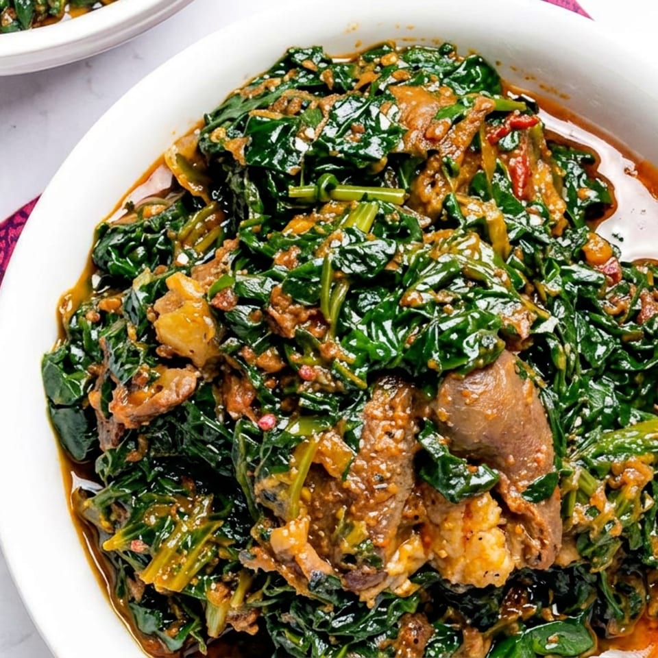 White serving bowl filled with sautéed leafy greens, mushrooms, and golden-brown pieces in a savory sauce, surrounded by rice and side dishes.