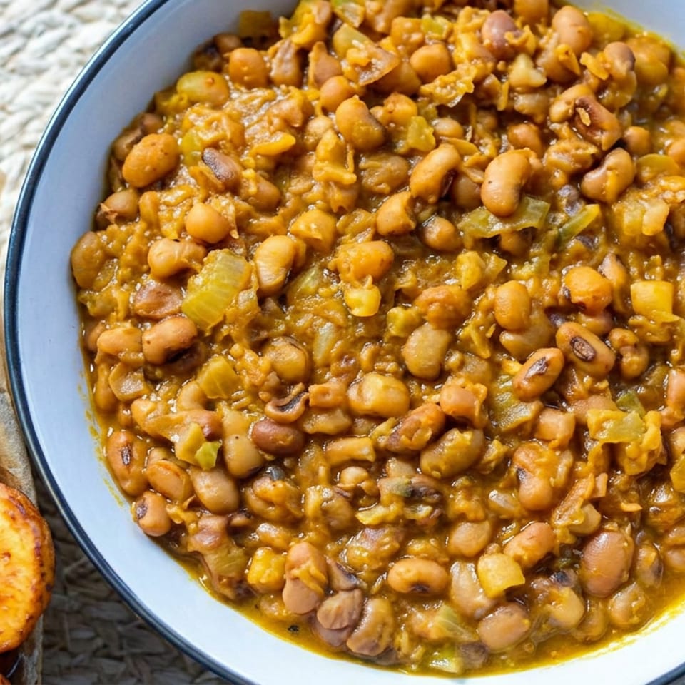Bowl of savory beans and rice served with golden fried plantain slices on a rustic woven placemat.